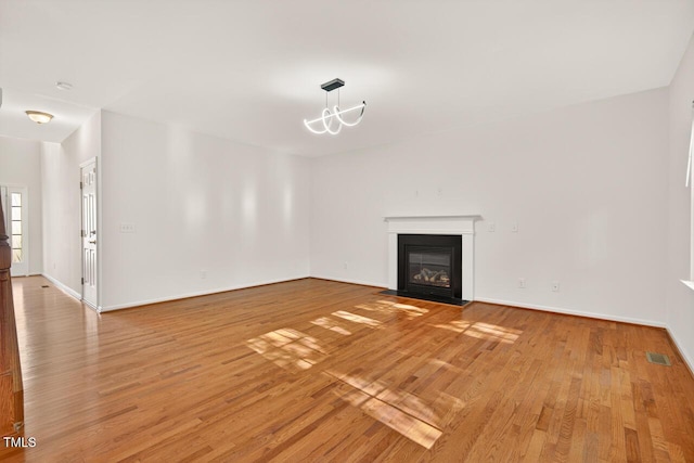 4518 Coral Dr, Durham, NC 27713 - unfurnished living room featuring light wood-style floors, a fireplace with flush hearth, and a chandelier