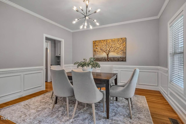 7269 Bedford Ridge Dr, Apex, NC 27539 - dining space featuring a chandelier, wood finished floors, ornamental molding, a wainscoted wall, and a decorative wall