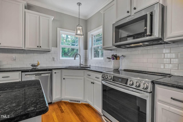 7269 Bedford Ridge Dr, Apex, NC 27539 - kitchen with appliances with stainless steel finishes, ornamental molding, light wood finished floors, hanging light fixtures, and white cabinetry