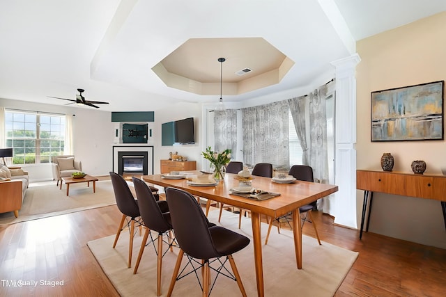 2486 Ingleside Dr, High Point, NC 27265 - dining space with a tray ceiling, a ceiling fan, a glass covered fireplace, light wood-style floors, and decorative columns