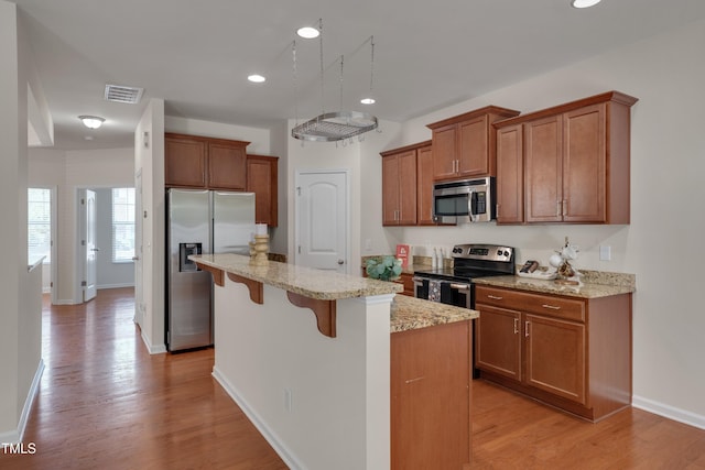 130 Holly Berry Ln, Durham, NC 27703 - kitchen with appliances with stainless steel finishes, brown cabinets, a kitchen breakfast bar, a kitchen island, and light wood-style flooring