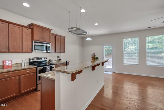 130 Holly Berry Ln, Durham, NC 27703 - kitchen featuring stainless steel appliances, brown cabinets, a kitchen breakfast bar, light wood-style flooring, and recessed lighting