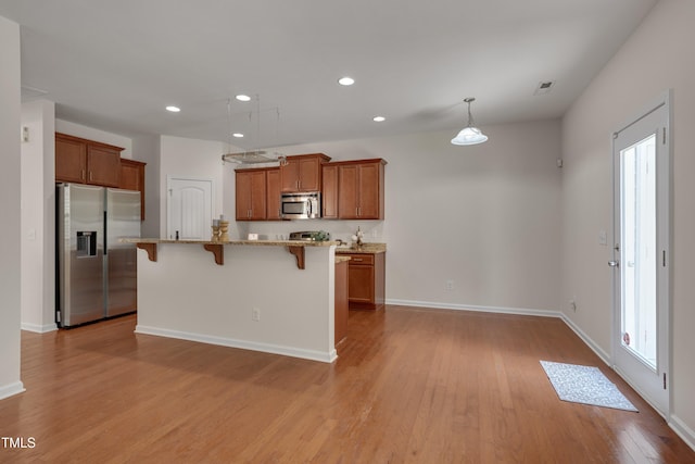 130 Holly Berry Ln, Durham, NC 27703 - kitchen featuring stainless steel appliances, brown cabinets, light wood-type flooring, a kitchen breakfast bar, and recessed lighting