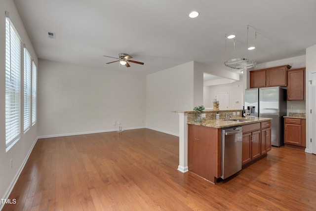 130 Holly Berry Ln, Durham, NC 27703 - kitchen featuring appliances with stainless steel finishes, light wood-type flooring, ceiling fan, brown cabinetry, and light stone counters