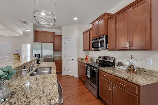 130 Holly Berry Ln, Durham, NC 27703 - kitchen featuring appliances with stainless steel finishes, dark wood finished floors, brown cabinetry, light stone countertops, and recessed lighting