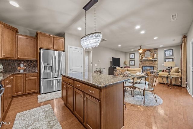 2505 Goldeneye Ct, Raleigh, NC 27606 - kitchen featuring a ceiling fan, a stone fireplace, stainless steel fridge, a kitchen island, and brown cabinets