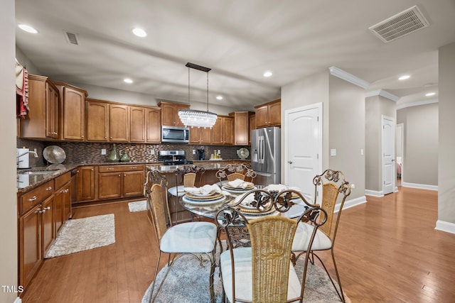 2505 Goldeneye Ct, Raleigh, NC 27606 - kitchen featuring crown molding, appliances with stainless steel finishes, tasteful backsplash, a center island, and wood finished floors