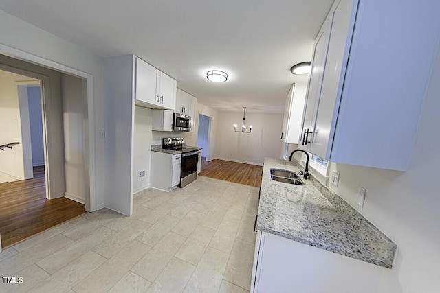 2309 Bertie Dr, Raleigh, NC 27610 - kitchen featuring a chandelier, appliances with stainless steel finishes, white cabinetry, light stone counters, and light wood-style flooring