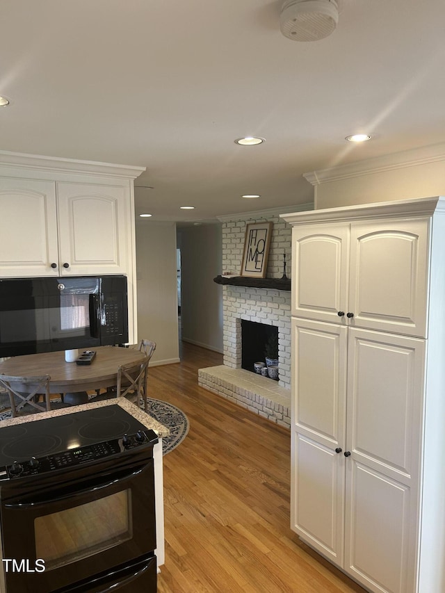 503 N Glen Dr, Raleigh, NC 27609 - kitchen with a fireplace, black appliances, crown molding, light wood-type flooring, and white cabinetry