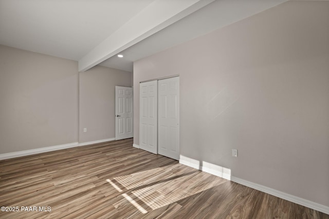 unfurnished bedroom with beam ceiling, wood-type flooring, and a closet