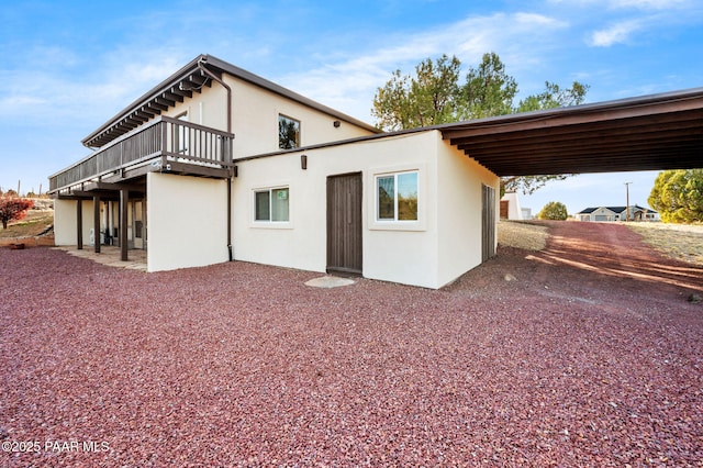 rear view of property with an attached carport, driveway, and stucco siding