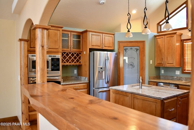 1284 Mcdonald Dr, Prescott, AZ 86303 - kitchen with stainless steel appliances, brown cabinetry, hanging light fixtures, lofted ceiling, and glass insert cabinets