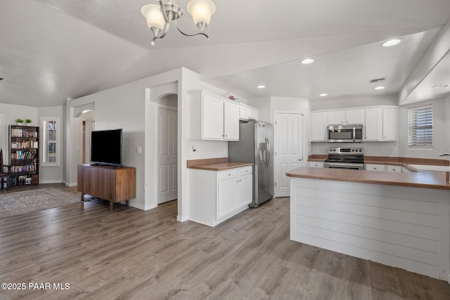 kitchen with white cabinets, lofted ceiling, kitchen peninsula, and stainless steel appliances