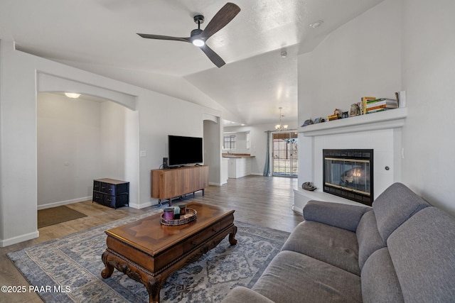 living room featuring a tile fireplace, ceiling fan with notable chandelier, lofted ceiling, and hardwood / wood-style flooring