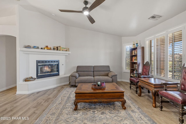 living room with a tiled fireplace, ceiling fan, hardwood / wood-style floors, and vaulted ceiling