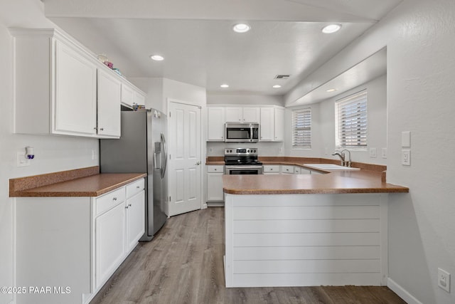 kitchen with kitchen peninsula, stainless steel appliances, sink, light hardwood / wood-style flooring, and white cabinets