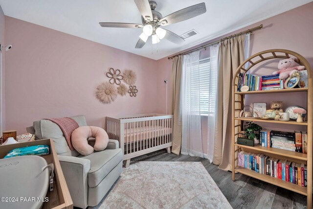 bedroom featuring ceiling fan, a crib, and hardwood / wood-style flooring