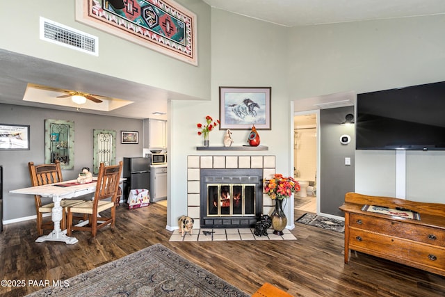 living room featuring a raised ceiling, visible vents, wood finished floors, a tile fireplace, and baseboards