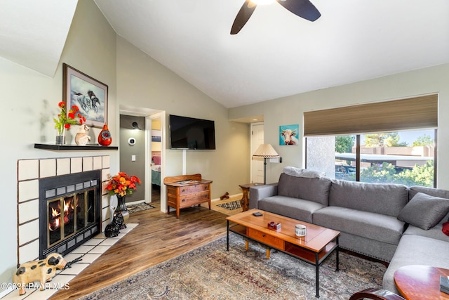 living area featuring ceiling fan, a fireplace, wood finished floors, baseboards, and vaulted ceiling