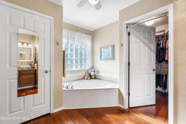 bathroom with hardwood / wood-style floors, vanity, ceiling fan, and a tub