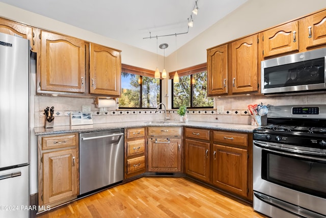 kitchen with sink, stainless steel appliances, vaulted ceiling, decorative backsplash, and light wood-type flooring