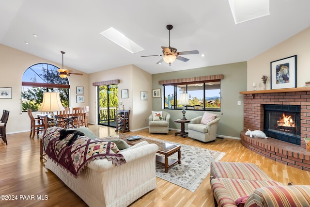 living room with ceiling fan, lofted ceiling with skylight, a fireplace, and light hardwood / wood-style flooring