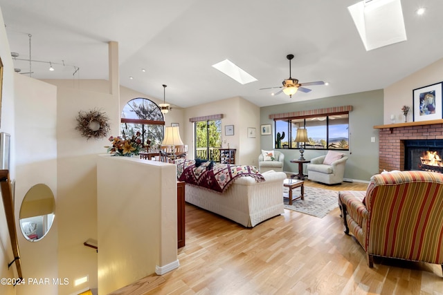 living room with a fireplace, light hardwood / wood-style floors, lofted ceiling with skylight, and ceiling fan