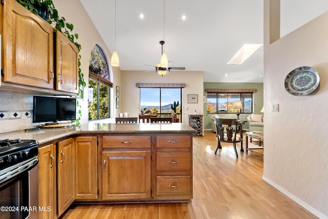 kitchen featuring stove, light wood-type flooring, tasteful backsplash, a skylight, and ceiling fan