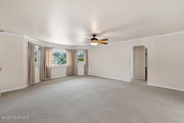 empty room with ornamental molding, baseboards, arched walkways, a ceiling fan, and light carpet