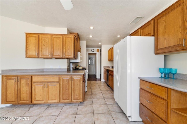kitchen with light tile patterned floors, visible vents, brown cabinets, and white appliances