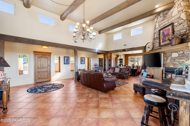 living room with a notable chandelier, light tile patterned flooring, a stone fireplace, and beam ceiling