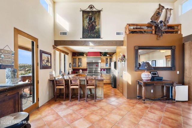 kitchen featuring kitchen peninsula, stainless steel fridge, wall chimney range hood, a high ceiling, and a breakfast bar area