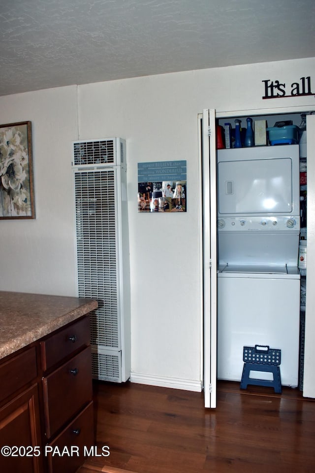 kitchen with a heating unit, dark wood finished floors, dark brown cabinetry, stacked washing maching and dryer, and a textured ceiling