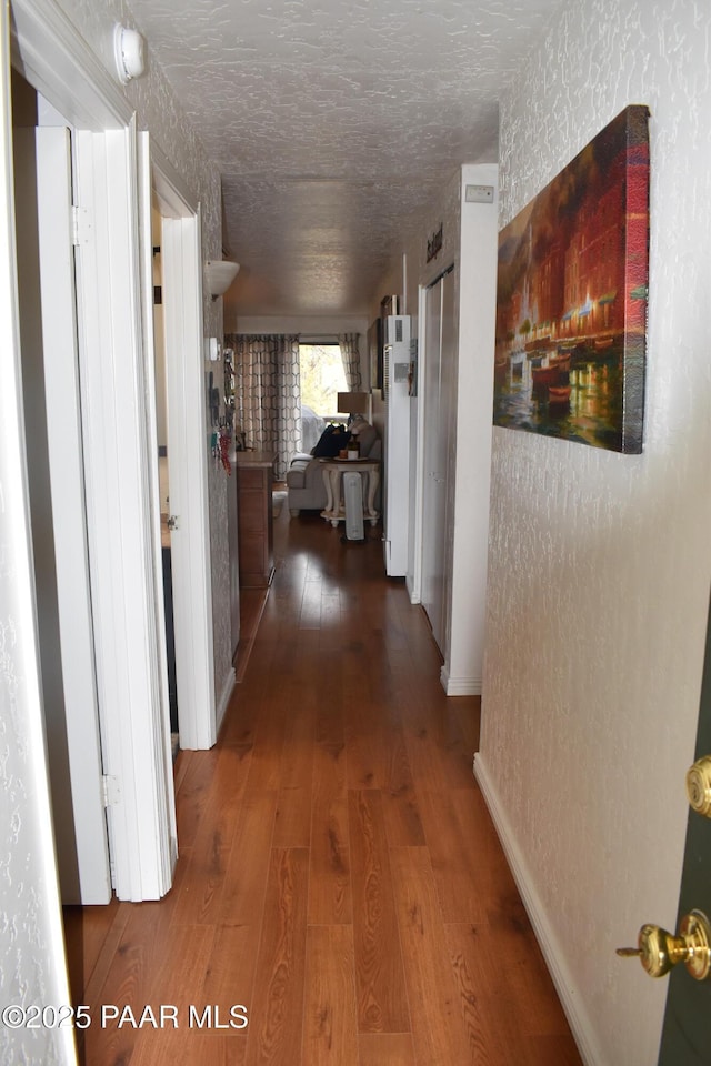 hallway with hardwood / wood-style floors, a textured wall, baseboards, and a textured ceiling