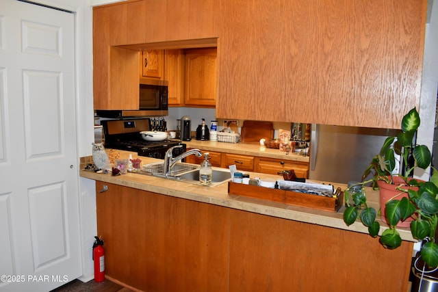 kitchen featuring stainless steel microwave, range with gas cooktop, light countertops, brown cabinets, and a sink