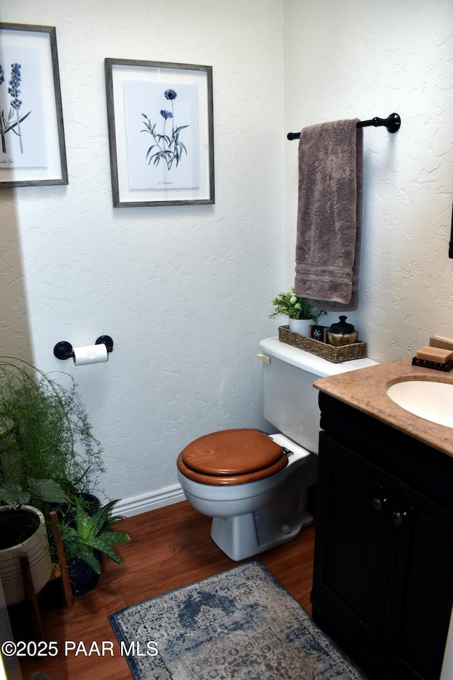 bathroom with toilet, vanity, a textured wall, and wood finished floors