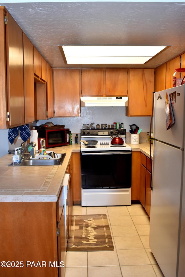 kitchen with light tile patterned flooring, freestanding refrigerator, a sink, range with electric cooktop, and under cabinet range hood