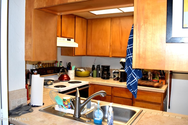 kitchen with under cabinet range hood, brown cabinetry, light countertops, and electric stove