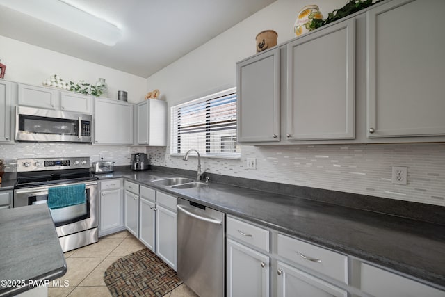 kitchen with dark countertops, backsplash, light tile patterned floors, stainless steel appliances, and a sink