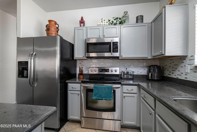 kitchen featuring light tile patterned floors, stainless steel appliances, gray cabinetry, and decorative backsplash