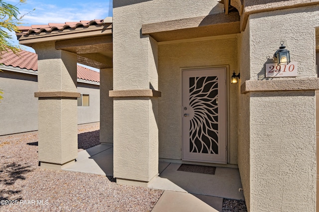 view of exterior entry with stucco siding and a tiled roof