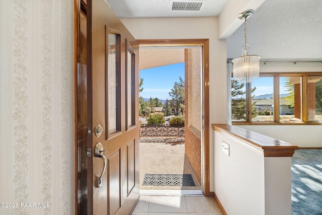 doorway to outside featuring visible vents, a textured ceiling, baseboards, and light tile patterned flooring