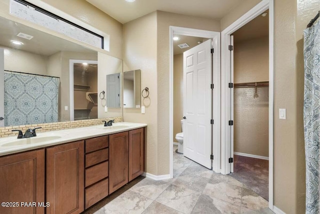 bathroom featuring toilet, a walk in closet, and a sink