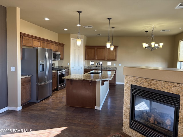 kitchen with appliances with stainless steel finishes, a kitchen breakfast bar, hanging light fixtures, light stone counters, and a center island with sink