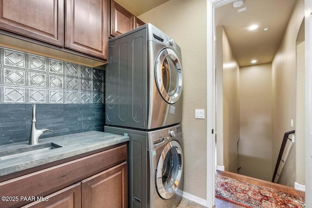 clothes washing area featuring stacked washing maching and dryer, a sink, cabinet space, and baseboards