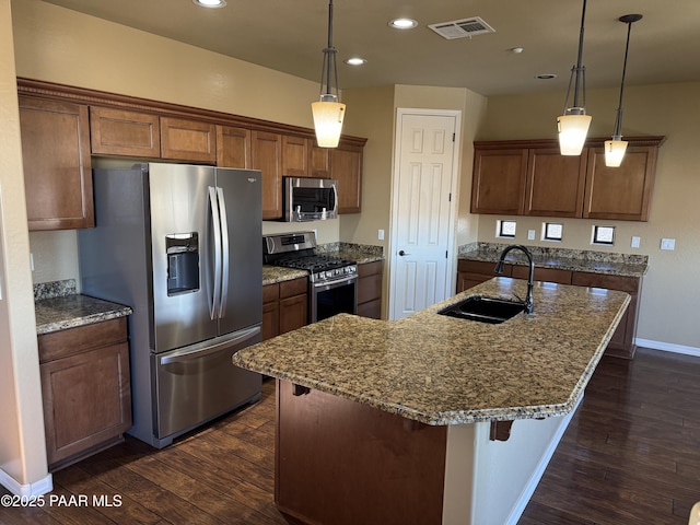 kitchen with decorative light fixtures, sink, appliances with stainless steel finishes, and a center island with sink