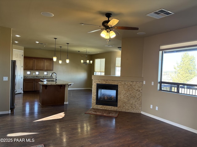 kitchen featuring decorative light fixtures, a center island with sink, dark wood-type flooring, black refrigerator, and light stone counters