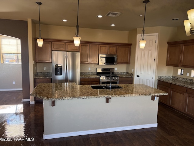 kitchen with appliances with stainless steel finishes, pendant lighting, a kitchen bar, and a kitchen island with sink