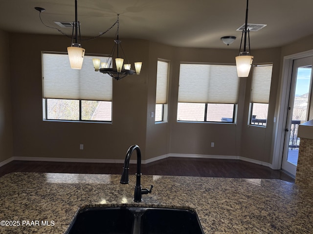 kitchen with a notable chandelier, dark hardwood / wood-style flooring, dark stone countertops, pendant lighting, and sink