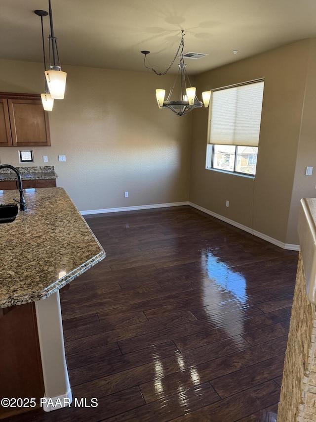 kitchen featuring pendant lighting, sink, dark hardwood / wood-style flooring, light stone counters, and a chandelier